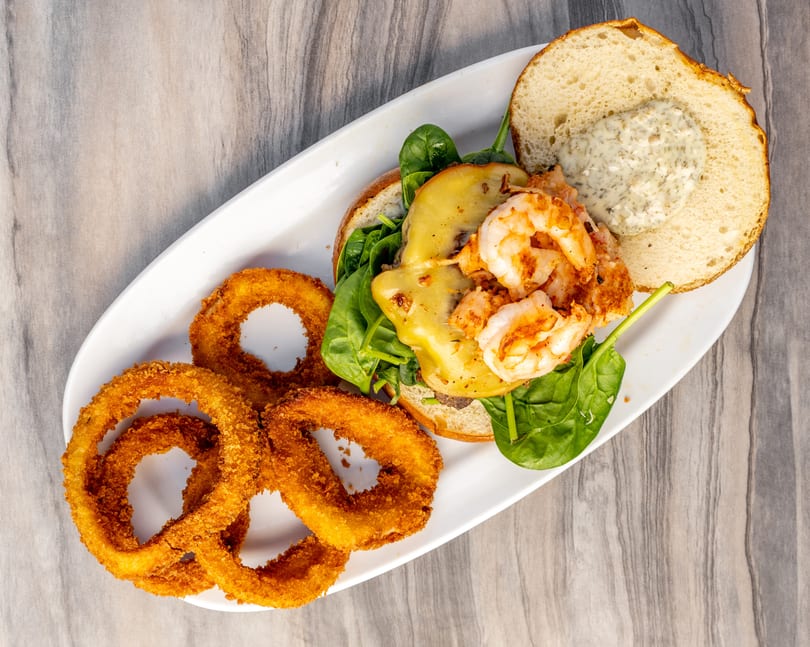 Overhead view of a shrimp burger with melted cheese, spinach, and a side of onion rings.
