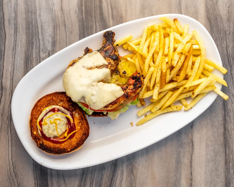 Grilled chicken sandwich with melted cheese, pickles, lettuce, tomato, and a side of fries.