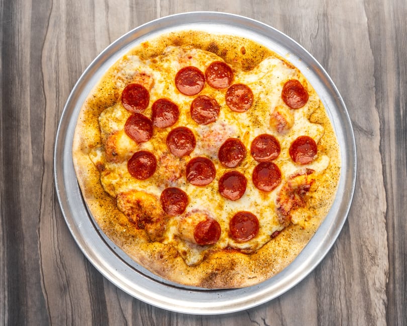 A whole pepperoni pizza with melted cheese on a metal tray, viewed from directly above.