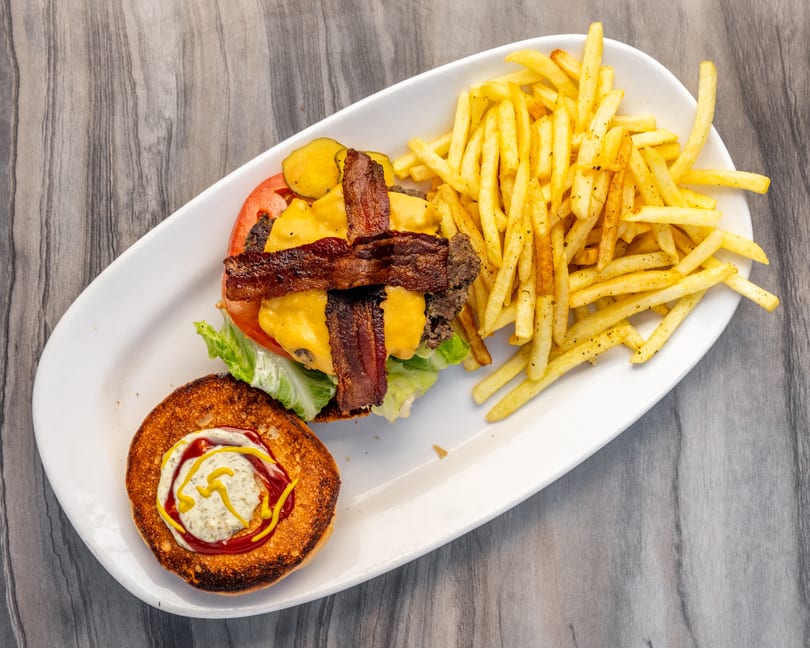 Overhead view of a bacon cheeseburger with lettuce, tomato, pickles, and a side of fries.