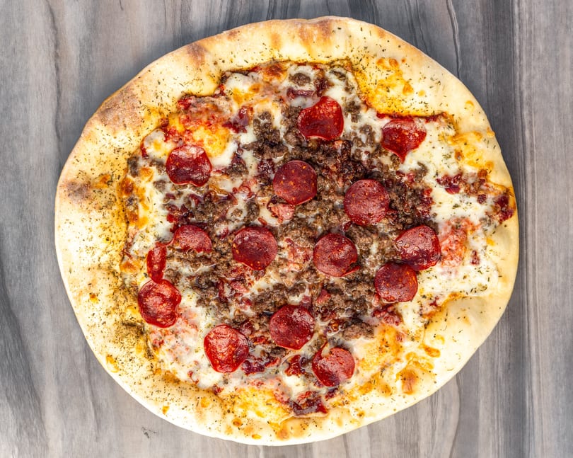 Overhead view of a whole pepperoni and ground beef pizza with melted cheese and herbs.