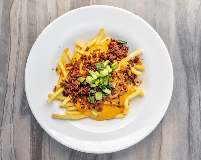 Loaded fries with melted cheese, bacon bits, caramelized onions, and chopped green onions on a white plate.