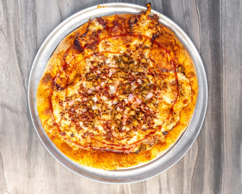 A whole BBQ chicken pizza with red onions on a metal tray, on a wooden table.