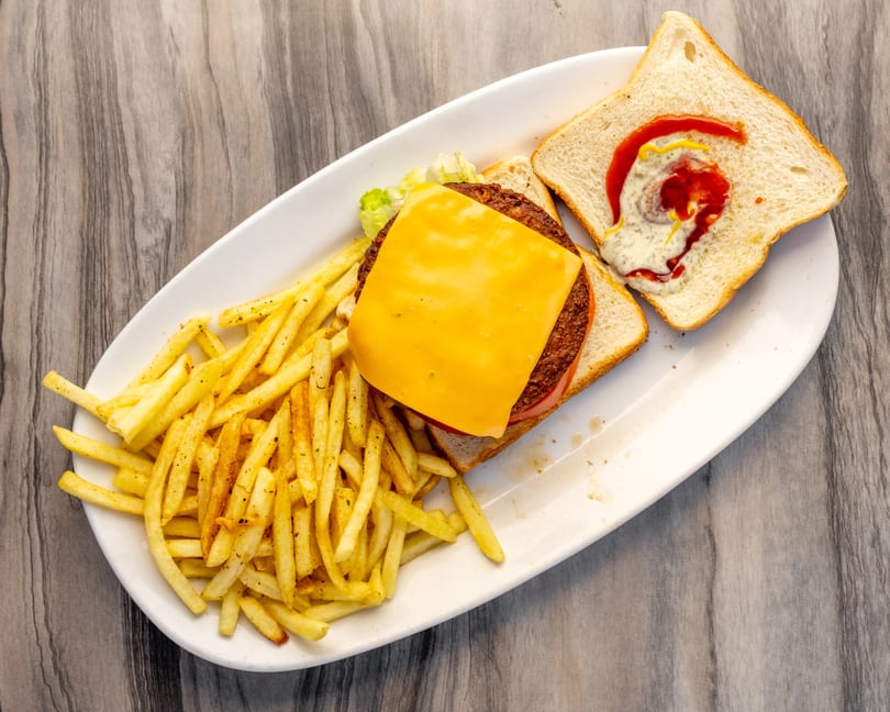 Open-faced burger with cheese, lettuce, tomato, and fries on a white plate.